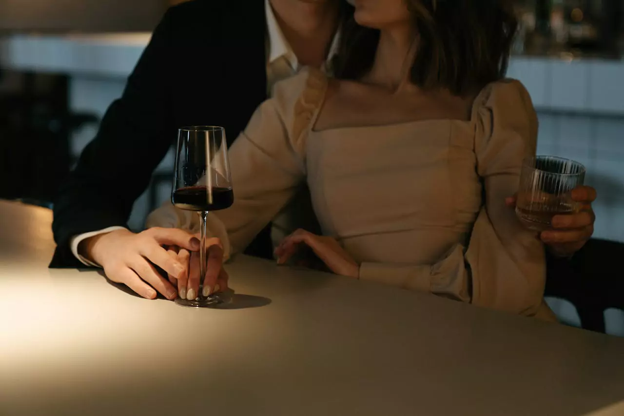 Un couple élégamment habillé partage un moment romantique dans un bar à l’ambiance tamisée, verre de vin à la main.