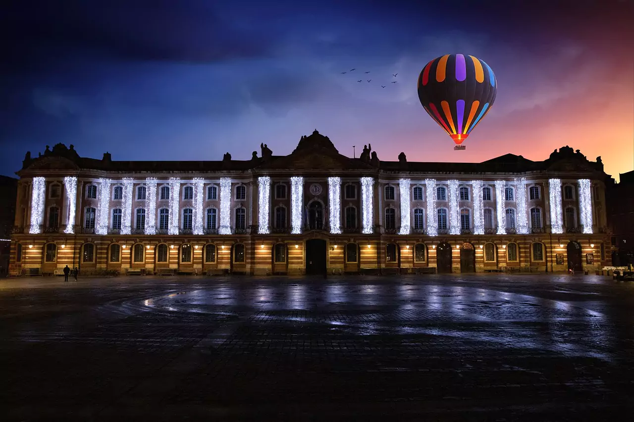 La place du Capitole illuminée de nuit avec une montgolfière flottant au-dessus, créant une atmosphère magique pour une soirée romantique.